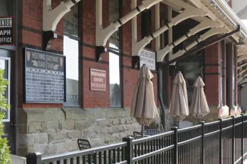 Historic train station exterior with brick walls, signage, and outdoor seating under umbrellas.