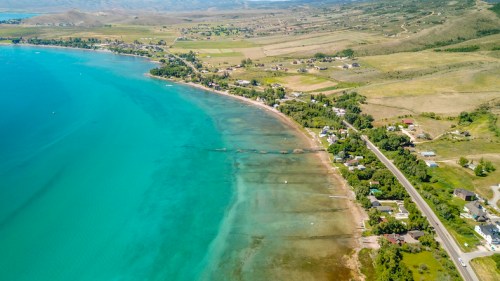 Aerial view of a serene lake with turquoise water, sandy shore, and green hills in the background.