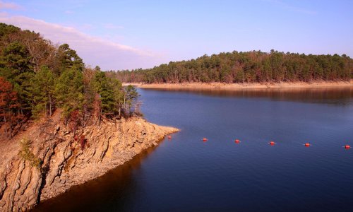 A serene lake surrounded by trees and rocky shores under a clear blue sky.