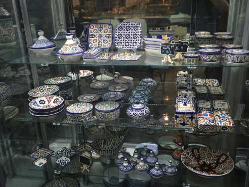 A display of colorful, intricately designed ceramic dishes and pottery in a glass cabinet.