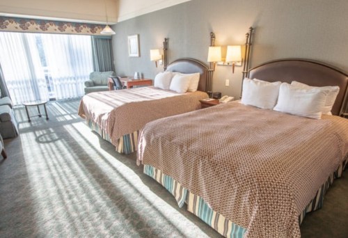 A hotel room with two beds, a seating area, and large windows letting in natural light.