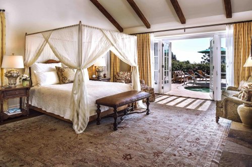 A spacious bedroom with a four-poster bed, elegant decor, and doors opening to a patio with outdoor seating.