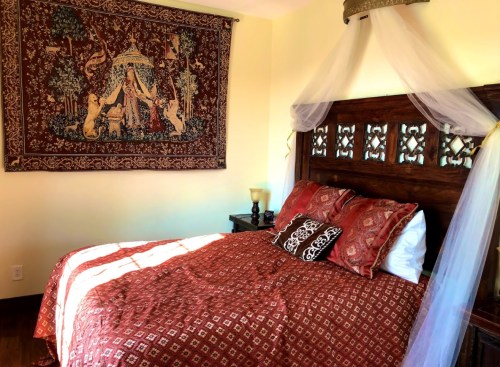 Cozy bedroom featuring a wooden bed with red patterned bedding and a decorative tapestry on the wall.