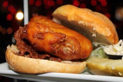 A close-up of a fried fish sandwich with a crispy fillet, served on a soft bun with pickles on the side.