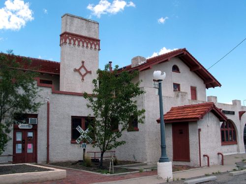 Historic building with a red-tiled roof, decorative elements, and a tree in front against a blue sky.