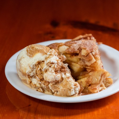 A slice of warm apple pie served with a scoop of vanilla ice cream on a white plate.