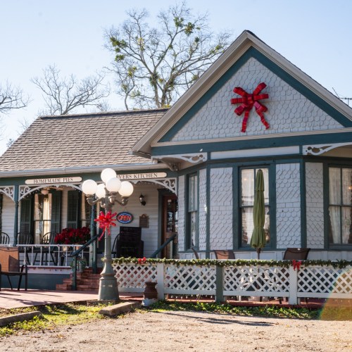 A charming house decorated with a large red bow, featuring a porch and festive holiday decorations.