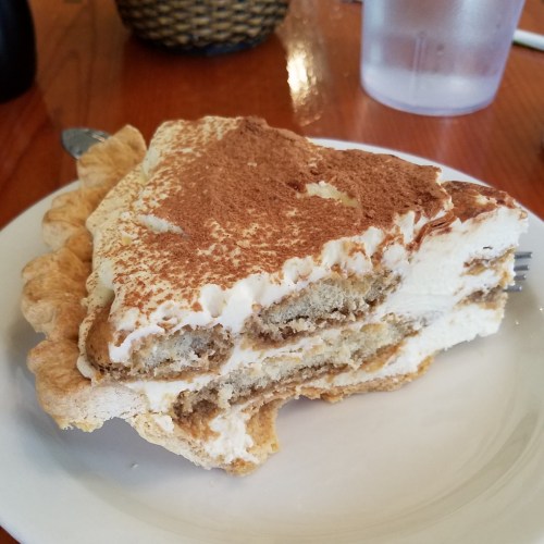 A slice of tiramisu pie with layers of cream and coffee-soaked cake on a white plate.
