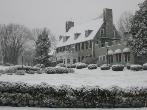 A snow-covered historic building surrounded by trees and a stone wall, creating a serene winter scene.