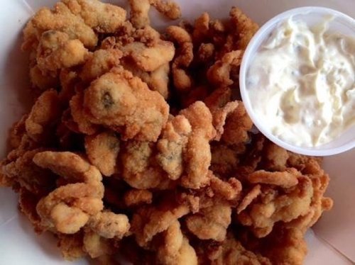 A plate of crispy fried oysters served with a small cup of creamy dipping sauce.