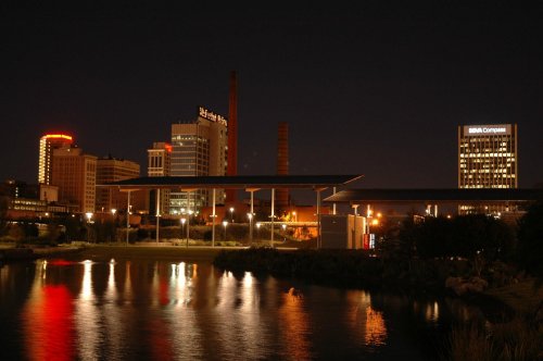 City skyline at night with illuminated buildings reflecting in a calm river.