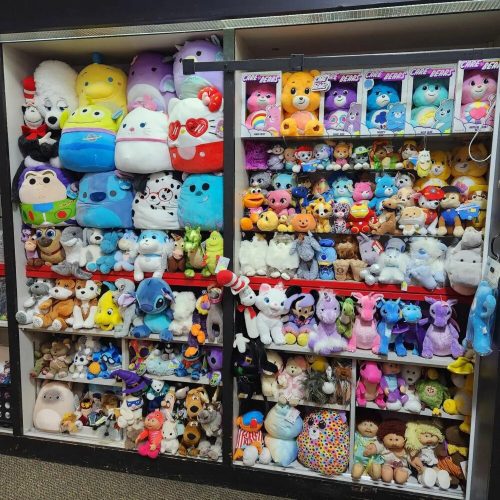 A colorful display of various plush toys, including animals, characters, and cute figures, neatly arranged on shelves.