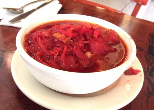 A bowl of rich red soup with shredded vegetables, served on a white plate, on a wooden table.