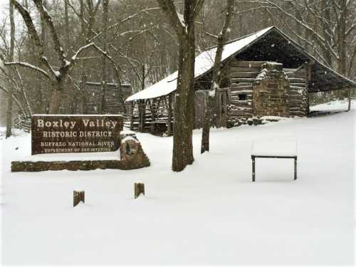 Snow-covered landscape featuring a historic sign for Boxley Valley and a rustic cabin in the background.