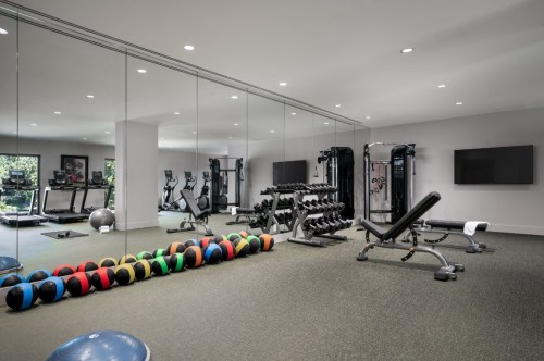 A modern gym with mirrors, weights, exercise machines, and colorful medicine balls on the floor.