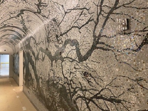 A mosaic-covered wall in a tunnel, featuring intricate tree branch patterns in black and white.