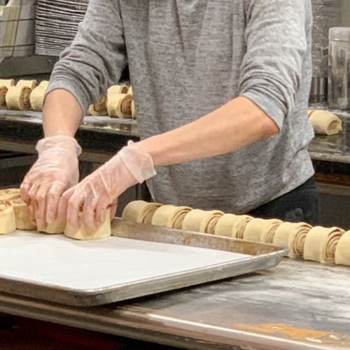 A person in gloves shapes dough on a baking tray in a kitchen setting.