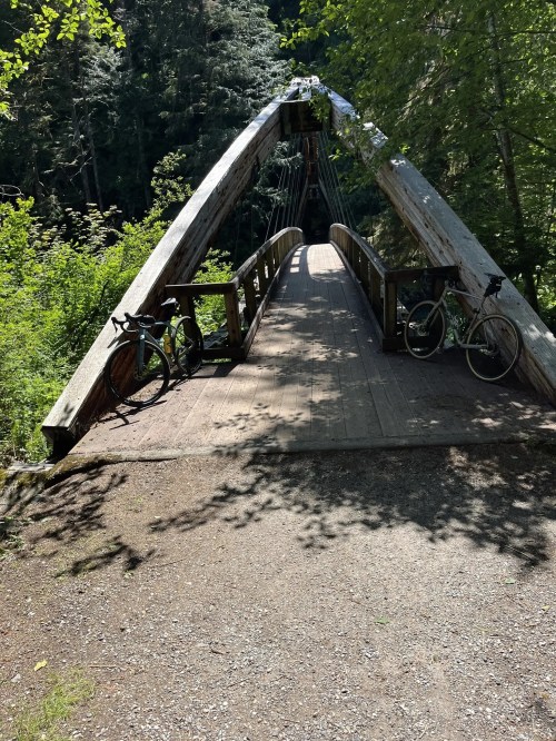 A wooden suspension bridge surrounded by lush greenery, with two bicycles parked on the side.