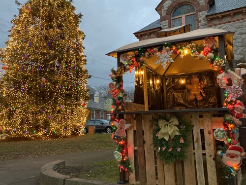 A festive scene featuring a decorated Christmas tree and a holiday kiosk adorned with lights and ornaments.