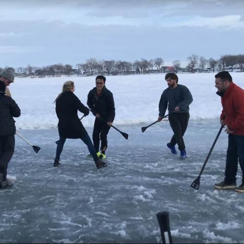 A group of people playing a game on ice, using sticks, with a snowy landscape in the background.