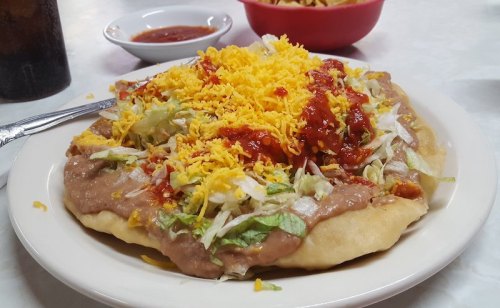 A plate of a large taco topped with lettuce, cheese, salsa, and refried beans, served with a side of sauce.