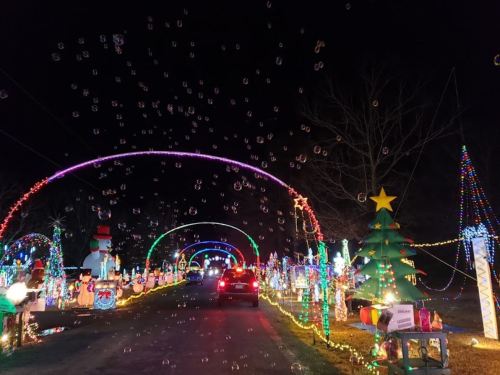 A festive night scene with colorful holiday lights, decorations, and bubbles floating above a car driving through.
