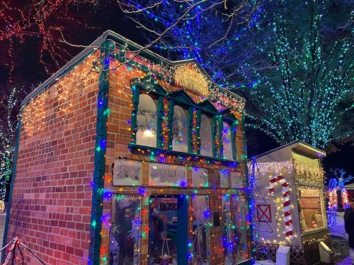 A festive scene featuring a brick building adorned with colorful holiday lights, surrounded by illuminated trees.