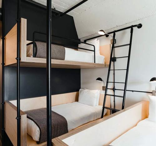 A modern bedroom with two bunk beds, featuring wooden frames and black metal accents, against a dark wall.