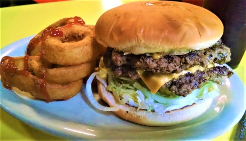 A double cheeseburger with lettuce and cheese, served with onion rings drizzled with ketchup on a blue plate.