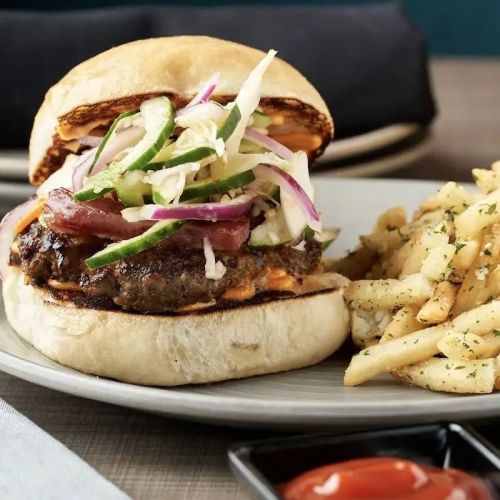 A juicy burger topped with lettuce, onions, and peppers, served with a side of seasoned fries and ketchup.
