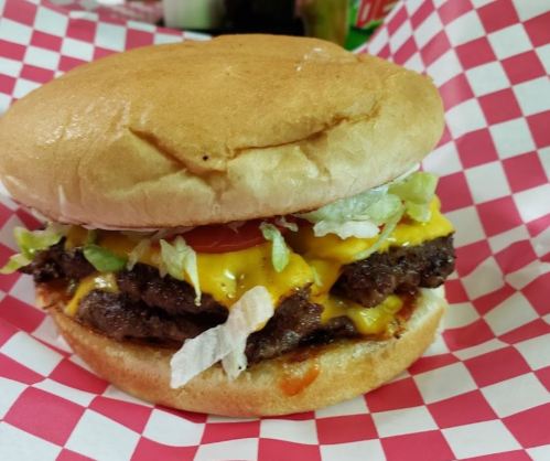 A juicy cheeseburger with lettuce, tomato, and pickles on a toasted bun, served in a red and white checkered wrapper.