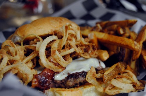 A close-up of a burger topped with crispy fried onions, served with a side of golden French fries.