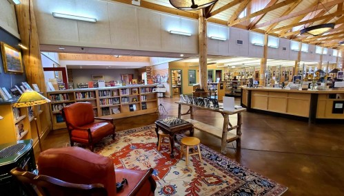 Cozy library interior with wooden beams, bookshelves, seating area, and a rug, creating a welcoming atmosphere.
