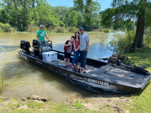 A family poses on a boat by a river, surrounded by greenery, with fishing gear and a cooler on board.