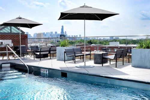 Rooftop pool area with lounge chairs and umbrellas, overlooking a city skyline on a sunny day.