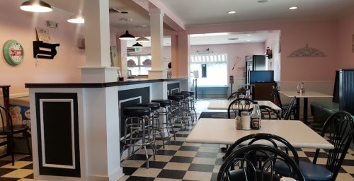 Interior of a cozy diner with pink walls, black and white checkered floor, tables, and bar seating.
