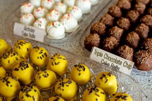 A display of colorful cake balls: yellow with sprinkles, white with frosting, and chocolate-coated varieties.