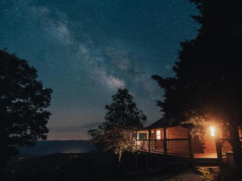 A cozy cabin illuminated at night, with the Milky Way shining brightly in the starry sky above.