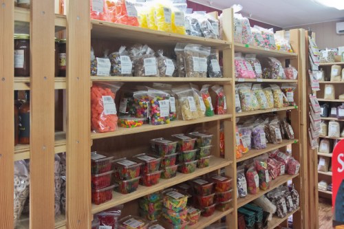 A colorful display of various candies and sweets in clear bags and containers on wooden shelves.