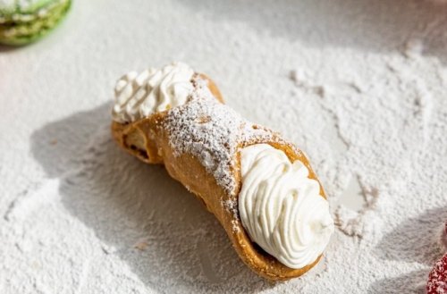 A delicious cannoli filled with creamy filling, dusted with powdered sugar, on a light surface.