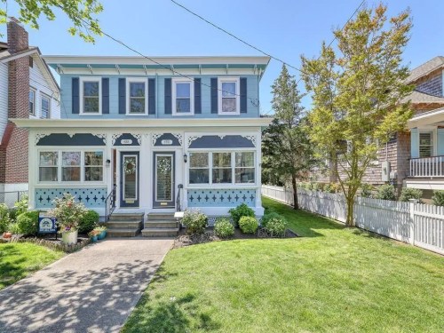 A charming blue and white duplex with a well-maintained lawn and decorative trim on a sunny day.