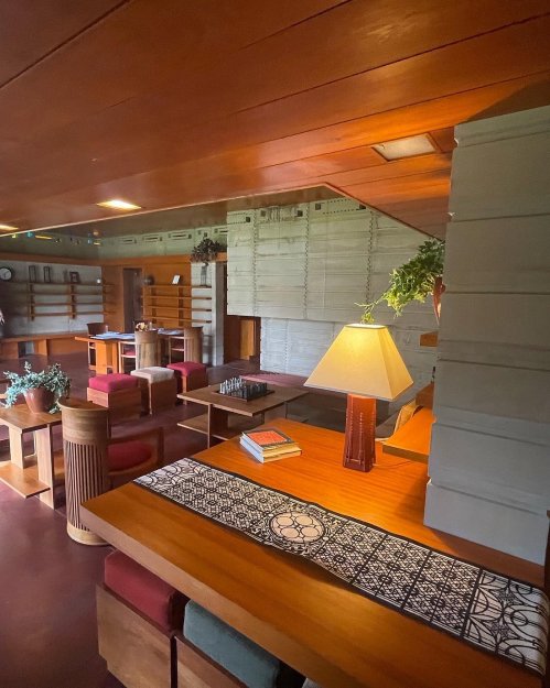 Interior of a modern room featuring wooden furniture, a lamp, plants, and a chess set, with a warm, inviting atmosphere.
