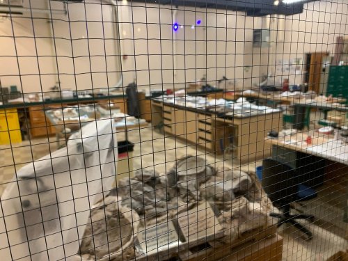 A view of a laboratory filled with tables, tools, and materials, seen through a wire mesh window.