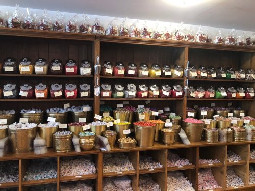 A colorful display of various candies in jars and containers on wooden shelves, with bags of sweets on top.