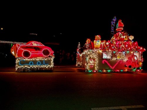 Colorful holiday parade floats decorated with lights, featuring a car and a festive scene with Santa and decorations.