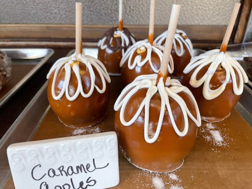 A tray of caramel apples decorated with white icing and wooden sticks, labeled "Caramel Apples."