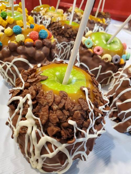 Close-up of chocolate-covered caramel apples topped with cereal, colorful candies, and drizzled with white chocolate.