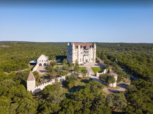 Aerial view of a large, castle-like building surrounded by greenery and trees in a rural landscape.