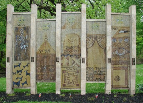 A mosaic display featuring various intricate designs and patterns, framed by tall stone pillars in a green park setting.