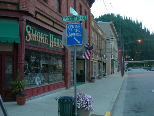 Street view featuring a sign for Bank Street and a "Center of the Universe" sign, with shops and mountains in the background.